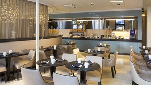 Un restaurante moderno con mesas redondas y sillas cómodas, una zona de bar con mostrador y un amplio ventanal con cortinas decorativas.