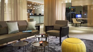 A modern hotel lobby with a sofa, armchairs, a yellow ottoman, and two small tables with candles. - Hôtel Oceania Le Jura Dijon (Dijon)