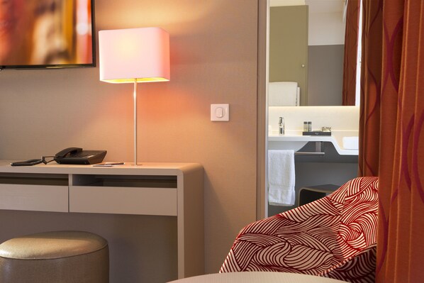 A hotel room with a desk, a lamp, a telephone, and a bed with patterned bedding.