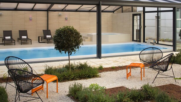 Zona de piscina exterior techada con sillas de descanso y un jacuzzi.