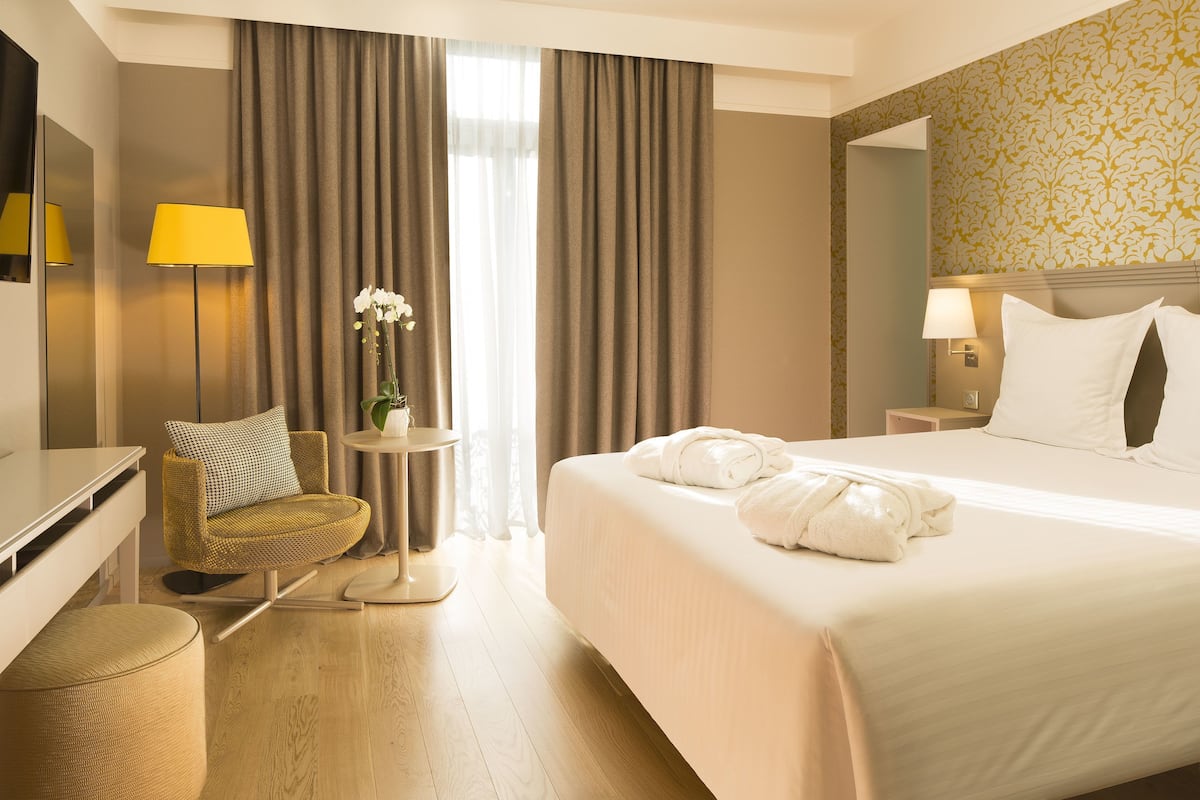 A hotel room with a bed, a chair, a desk, a lamp, and a small table with a plant.