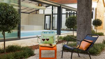 Un área de estar moderna al aire libre con piscina, una mesa de vidrio y dos copas de vino, y una silla de lounge.