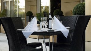A table set for two with a white tablecloth, two wine glasses, a bottle of wine, and a vase with a plant. - City Hotel Frankfurt am Main Bad Vilbel (Bad Vilbel)