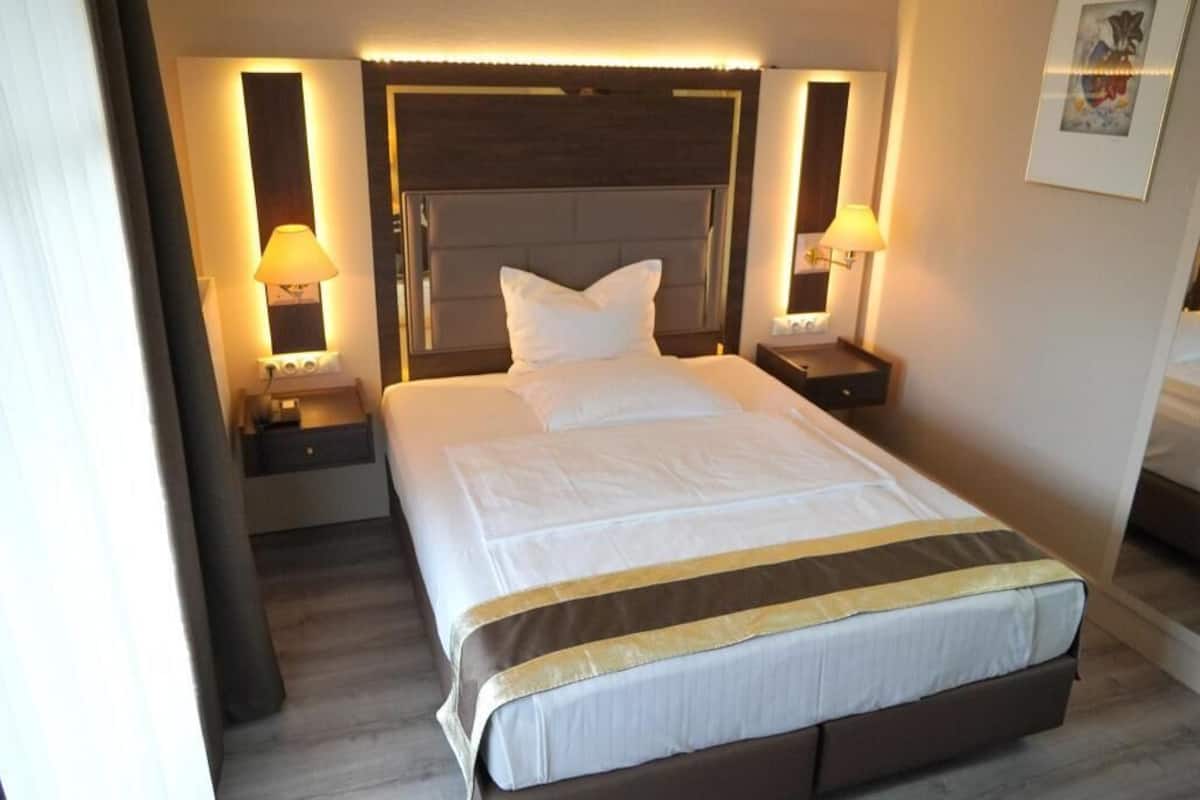 Ein Hotelzimmer mit einem großen Bett, zwei Nachttischen mit Lampen, einem Kopfteil und einem gerahmten Bild an der Wand.