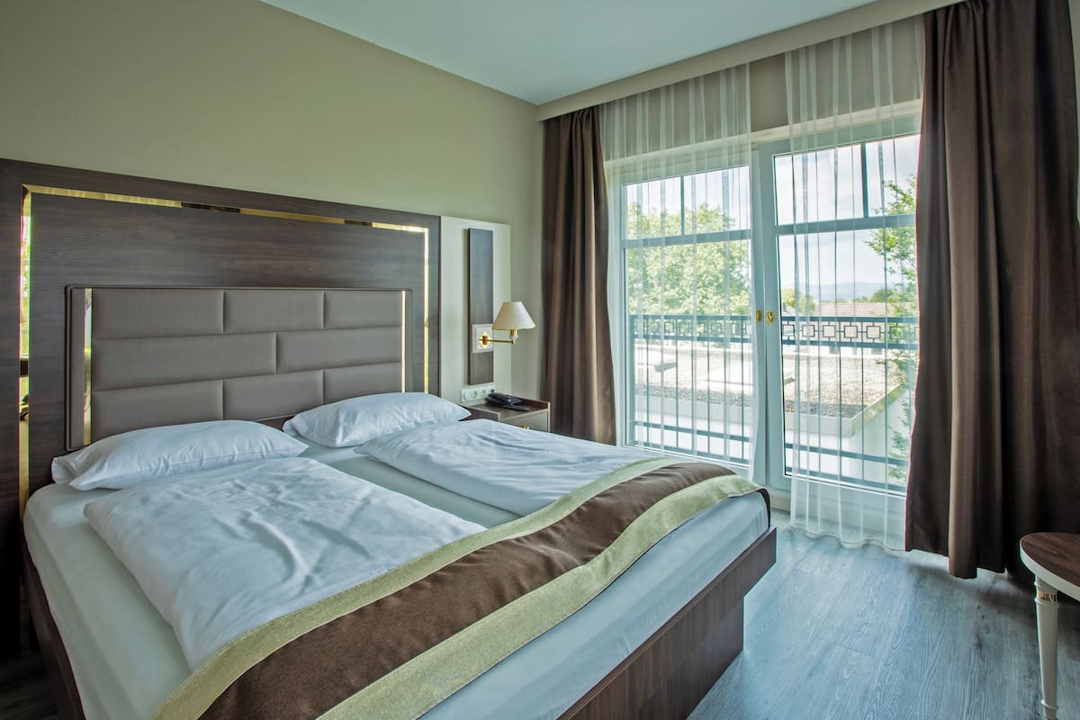 Une chambre d’hôtel avec un grand lit, une table de chevet, une lampe et une vue sur l’extérieur par une fenêtre.