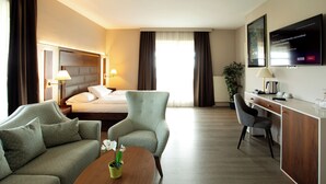 A hotel room with a bed, two armchairs, a desk, a coffee table, and a TV. - City Hotel Frankfurt am Main Bad Vilbel (Bad Vilbel)