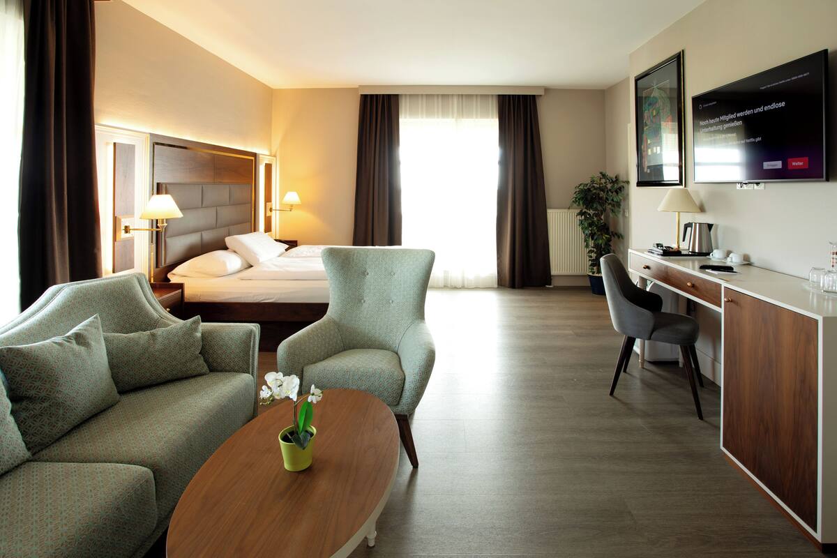 Une chambre d’hôtel comprenant un lit, deux fauteuils, un bureau, une table basse et un téléviseur.