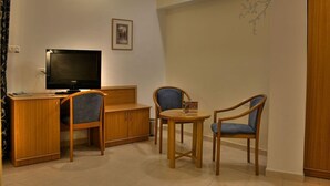 A compact living space with a wooden desk, a television, two chairs, and a small table. - The Golden Walls Hotel (Jerusalem)