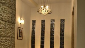 A hallway with two wooden chairs, a hanging chandelier, and a stone wall. - The Golden Walls Hotel (Jerusalem)