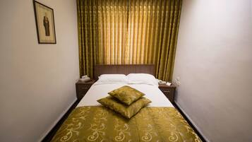 A narrow hotel room with a bed, a nightstand, a telephone, and a framed picture on the wall.
