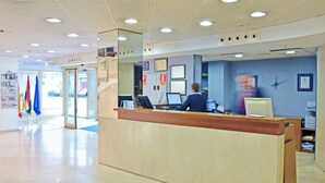 Un espace d’accueil avec un bureau en bois, un ordinateur et une personne assise.