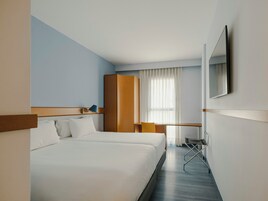 A hotel room with a bed, a desk, a chair, and a mirror.