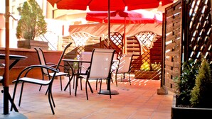 Un espace extérieur aménagé en terrasse, avec des chaises et des tables en métal, des parasols rouges et un mur en briques.