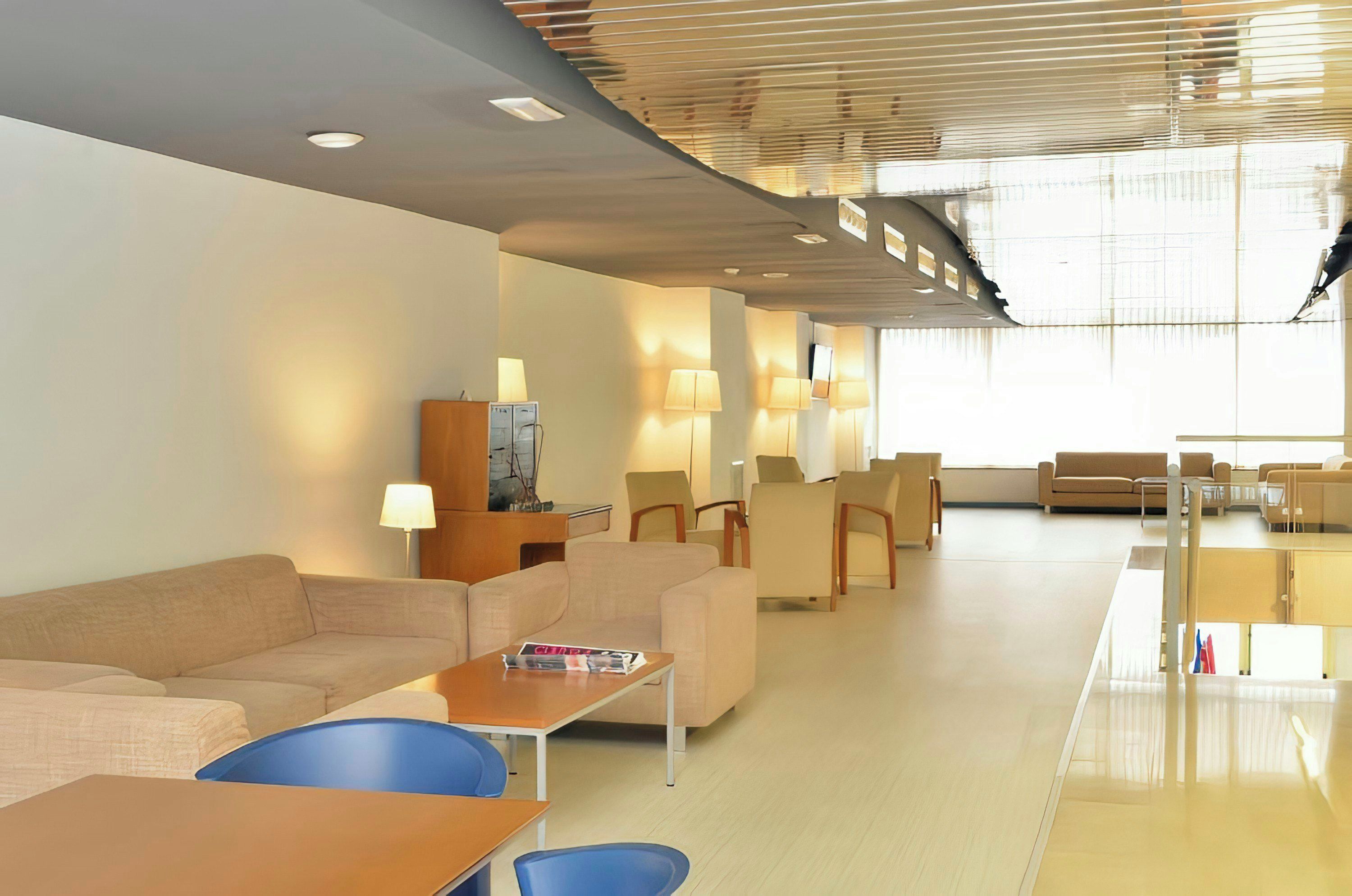 A modern hotel lobby with a seating area, a reception desk, and a large window providing natural light.