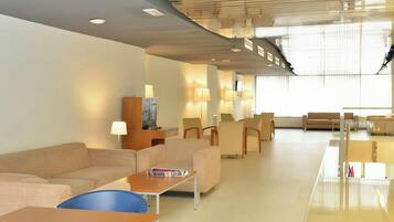 A modern hotel lobby with a seating area, a reception desk, and a large window providing natural light.
