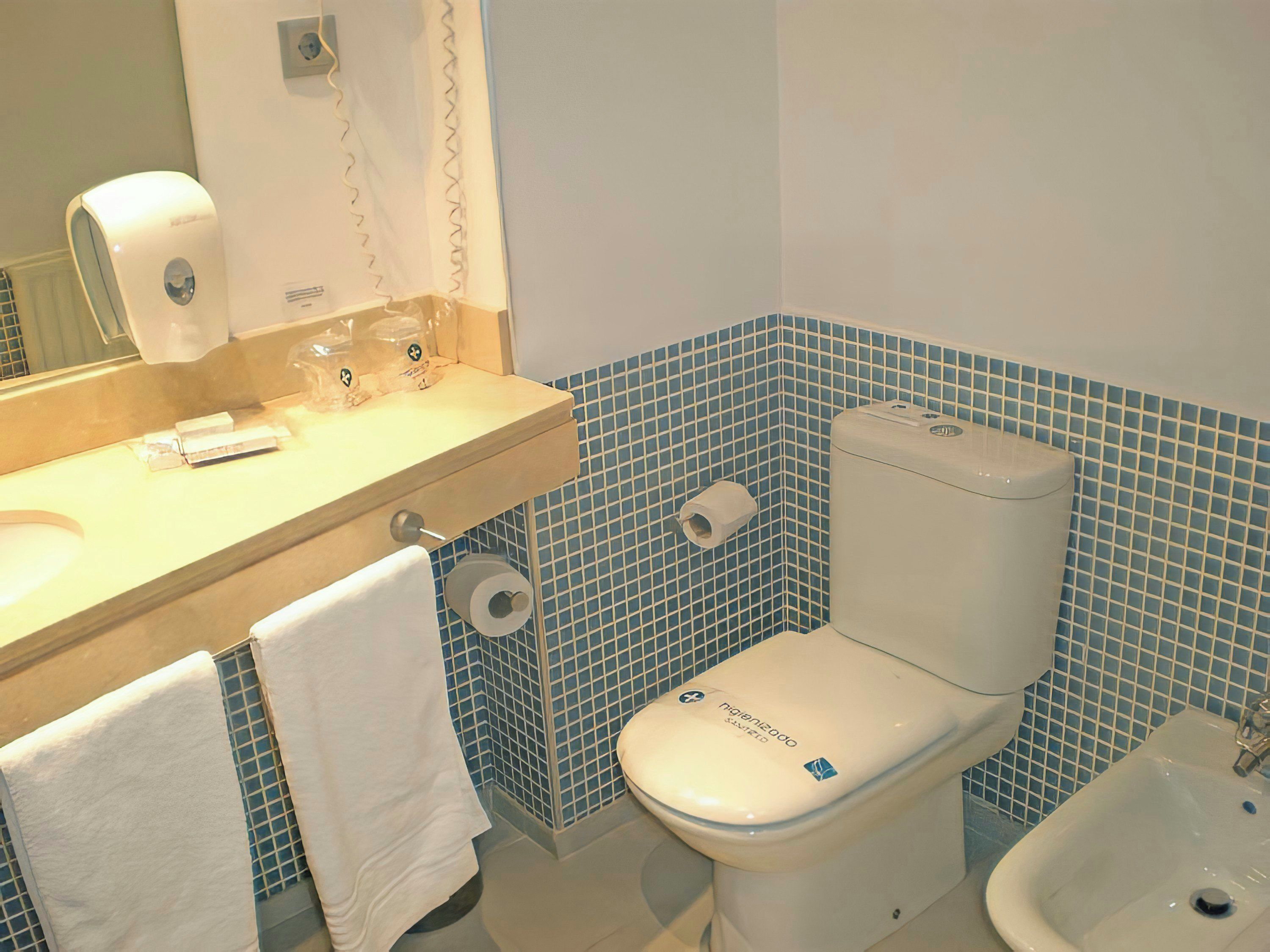 Casa de banho com sanita, bidé, lavatório e porta-toalhas.