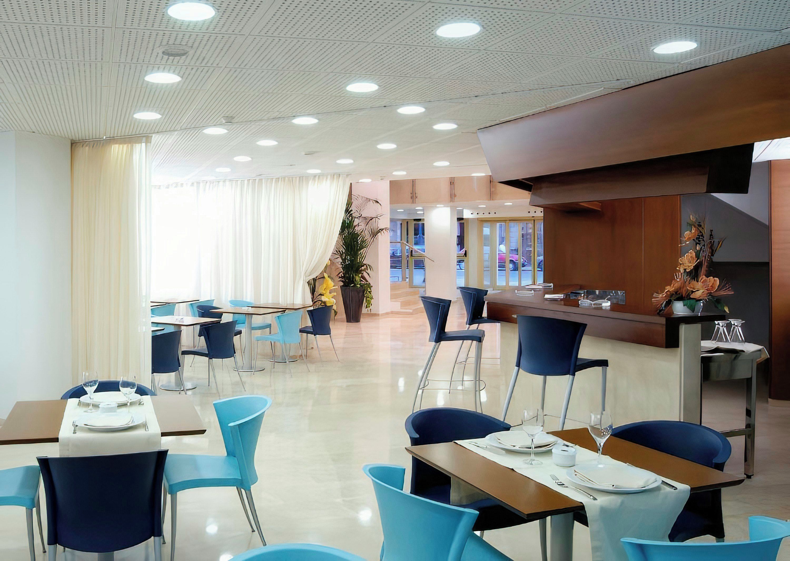 A modern dining area with multiple tables and chairs, a reception desk, and a large window with curtains.