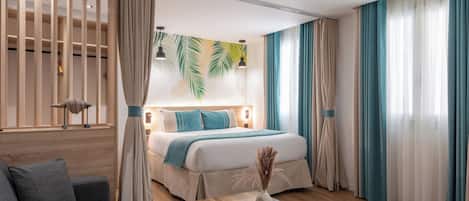 A modern hotel room with a bed, a sofa, a wooden coffee table, and a large window with curtains.