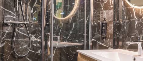Une salle de bain moderne avec une douche à parois de verre, un meuble-lavabo et des murs en marbre.
