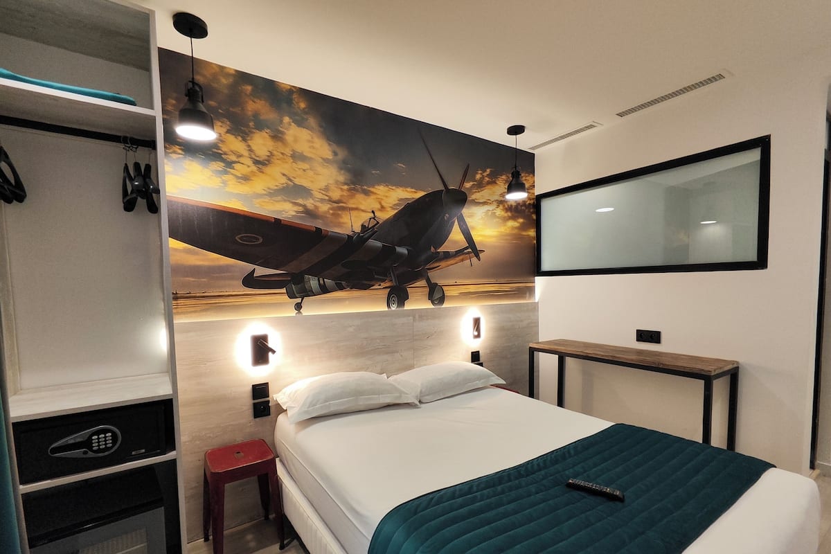 A hotel room with a bed, a desk, a TV, and a wall-mounted artwork of an airplane.
