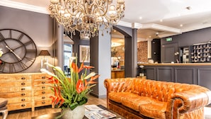 A modern lobby with a leather sofa, a wooden cabinet, a large clock, and a chandelier. - Atelier Montparnasse (Paris)