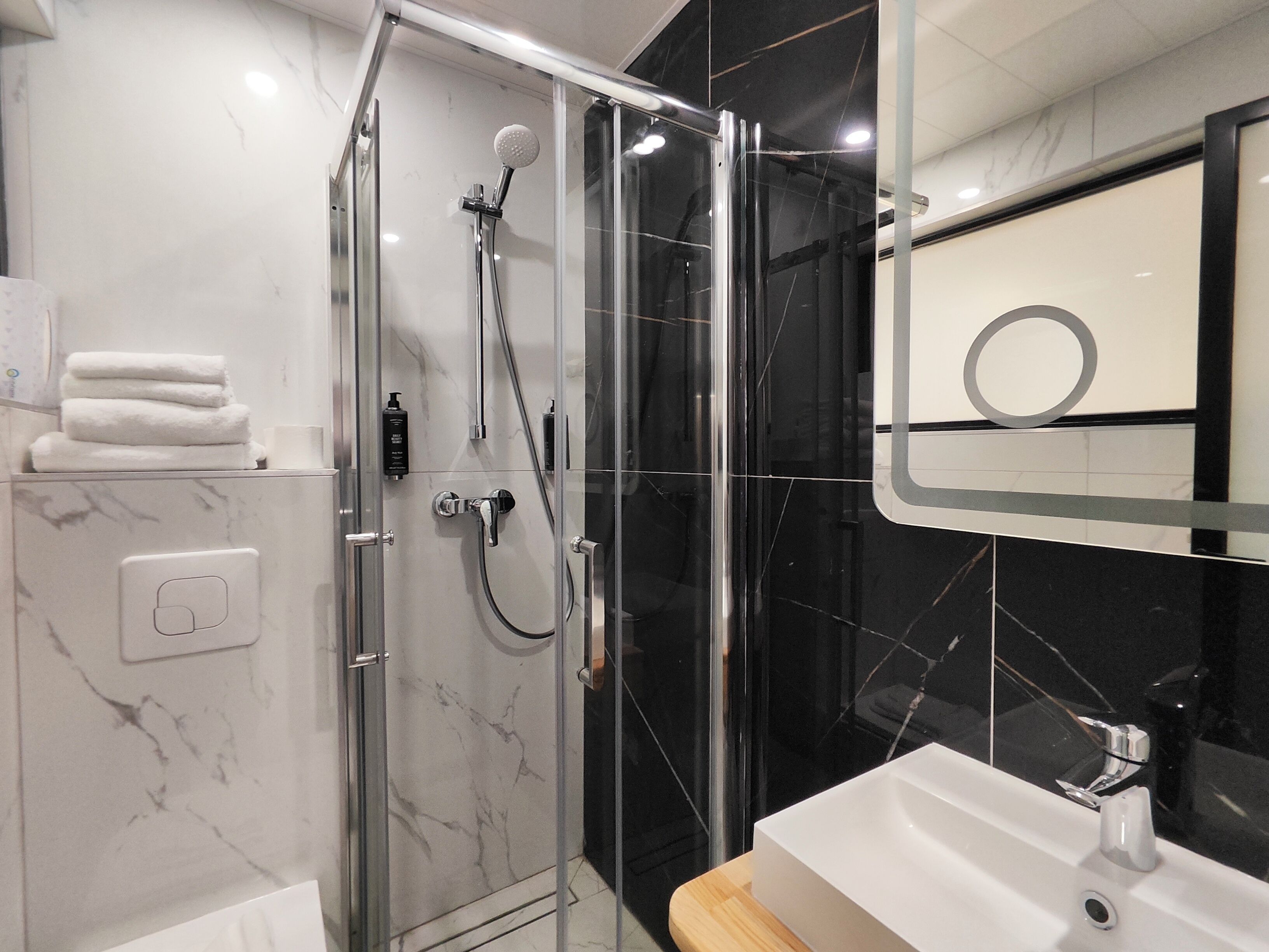 Un baño moderno con ducha de vidrio, un lavamanos blanco y un espejo con marco circular.