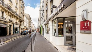 A street view with a hotel entrance, a pedestrian walkway, and various storefronts. - Atelier Montparnasse (Paris)