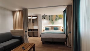 A hotel room with a bed, a sofa, a wooden coffee table, a wardrobe, and a bathroom visible in the background. - Atelier Montparnasse (Paris)