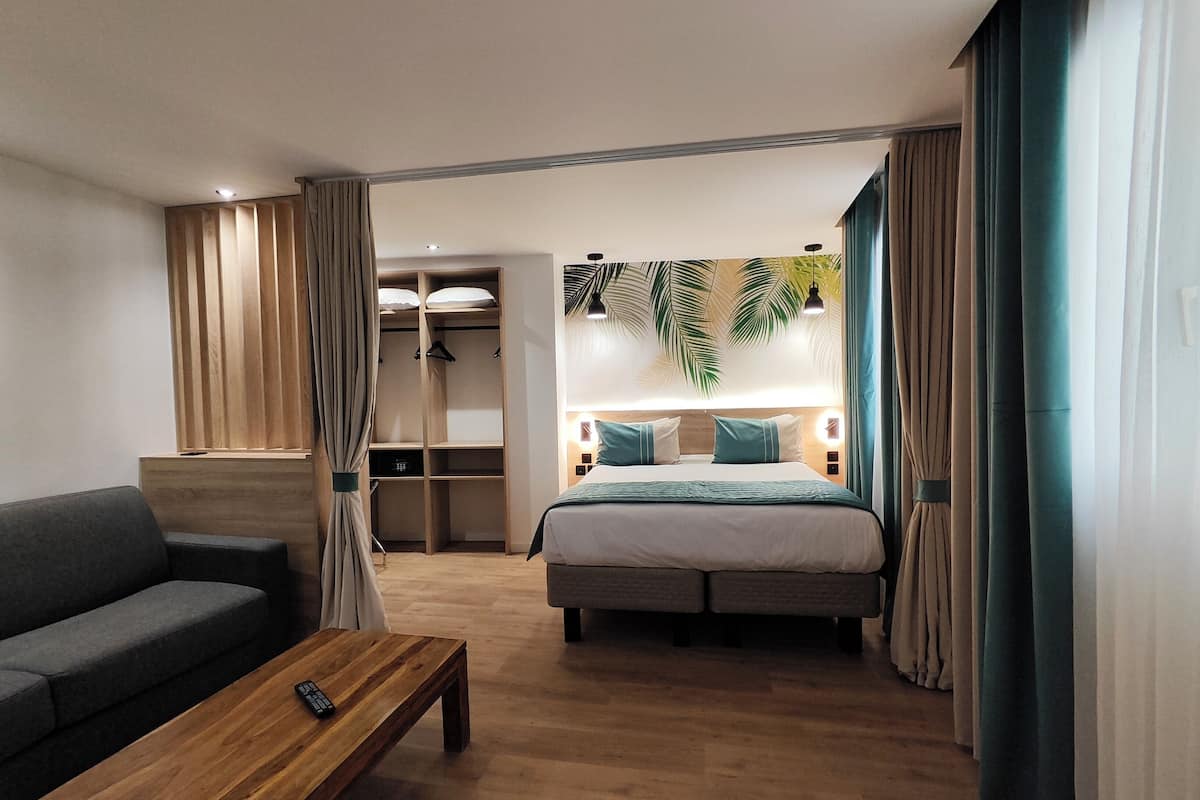 A hotel room with a bed, a sofa, a wooden coffee table, a wardrobe, and a bathroom visible through an open door.