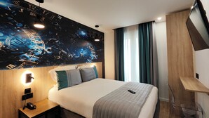 A modern hotel room with a large bed, a headboard with a space-themed mural, a bedside table with a lamp, and a TV mounted on the wall. - Atelier Montparnasse (Paris)