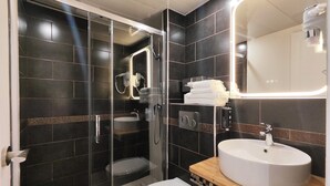 A modern bathroom with a glass-enclosed shower, a white toilet, and a wooden vanity with a white sink. - Atelier Montparnasse (Paris)