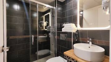 A modern bathroom with a glass-enclosed shower, a white toilet, and a wooden vanity with a white sink.