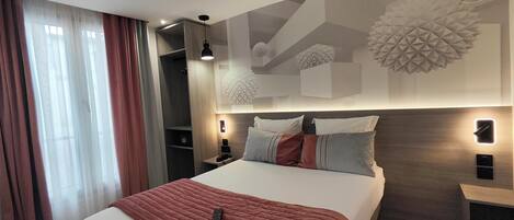 Une chambre d’hôtel moderne avec un grand lit, une table de chevet, une petite table d’appoint, une lampe fixée au mur et un panneau décoratif mural.