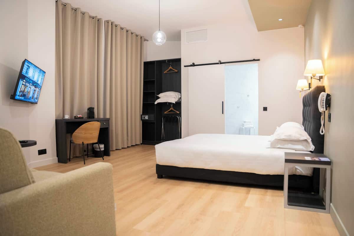 Quarto de hotel moderno com cama, escrivaninha, cadeira, guarda-roupa e televisão.