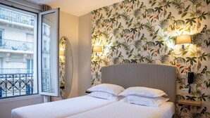 Ein Hotelzimmer mit zwei Betten, einem großen Fenster mit Blick auf ein Gebäude und floralem Wandpapier.
