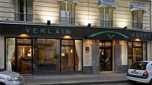 Eine Hotelansicht mit großen Glasfenstern, einem gut sichtbaren 'VERLAIN HOTEL'-Schild und einem parkenden Auto auf der Straße.