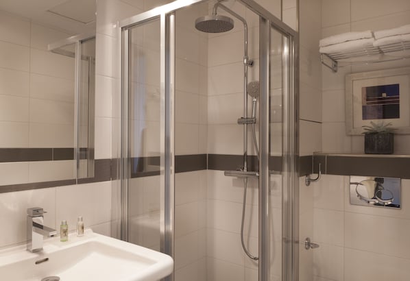 Un baño moderno con ducha de vidrio, un lavamanos con dos botellas de jabón y un perchero con toallas dobladas.