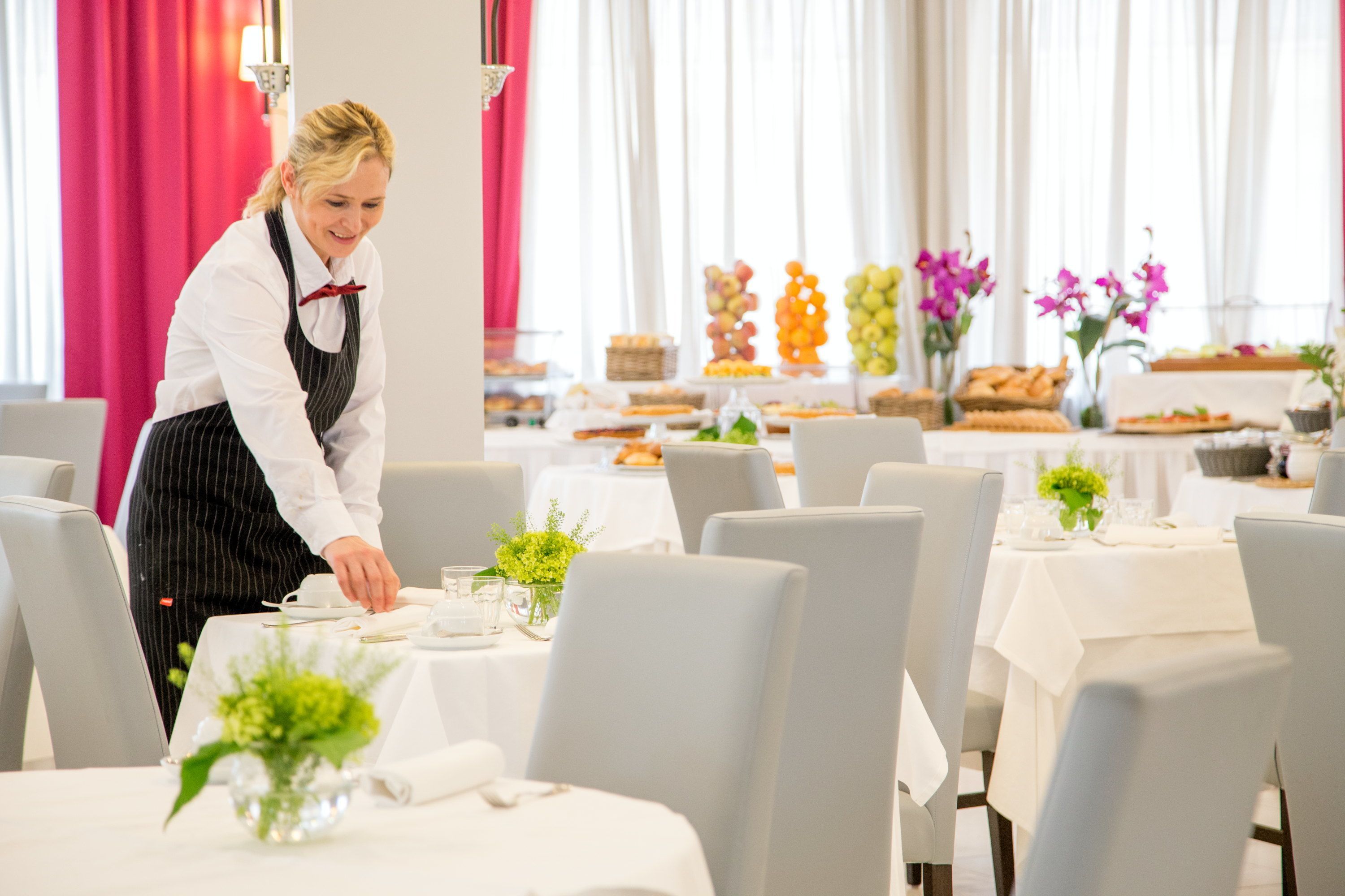 A restaurant with white tablecloths, neatly arranged chairs, and a variety of food displays in the background.