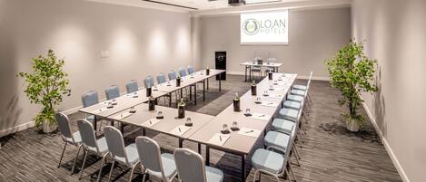 A conference room with a long table, chairs, and a projector screen displaying "LOAN HOTELS".