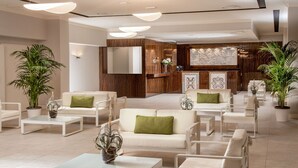 A spacious lobby with a modern design, featuring a central seating area with white sofas and armchairs, surrounded by potted plants. - Hotel Cristoforo Colombo (Rome)