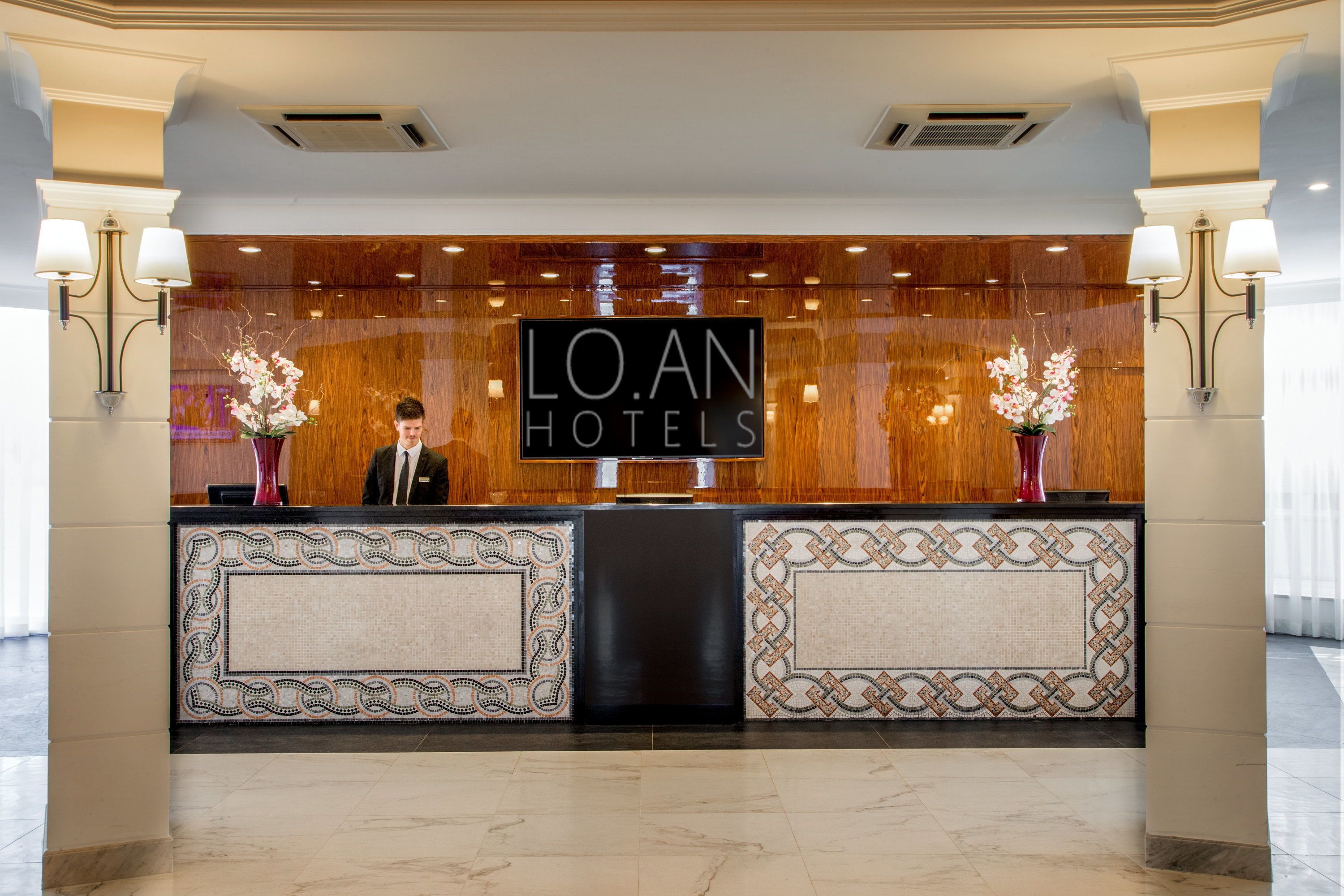 Ein Empfangstresen mit einem Schild, auf dem 'LOAN HOTELS' steht, und zwei Vasen mit Blumen.