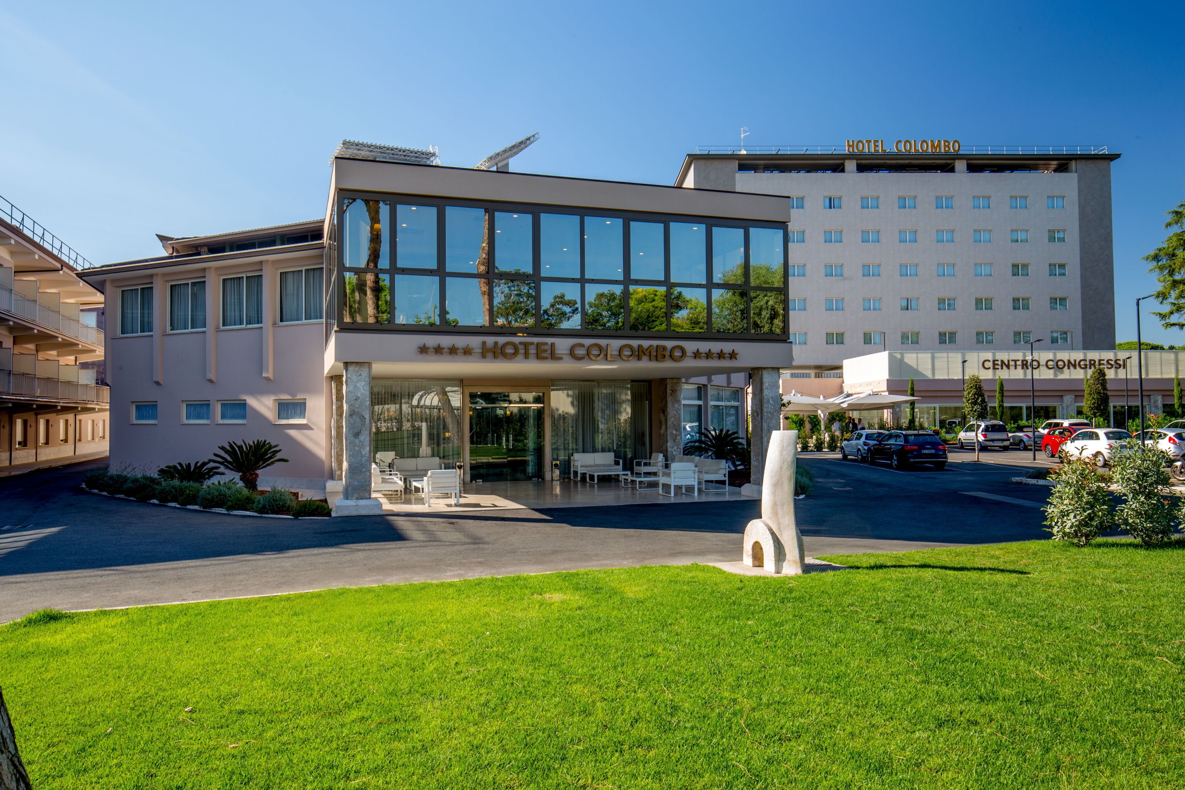 A modern hotel with a glass facade, a rooftop terrace, and a parking area.