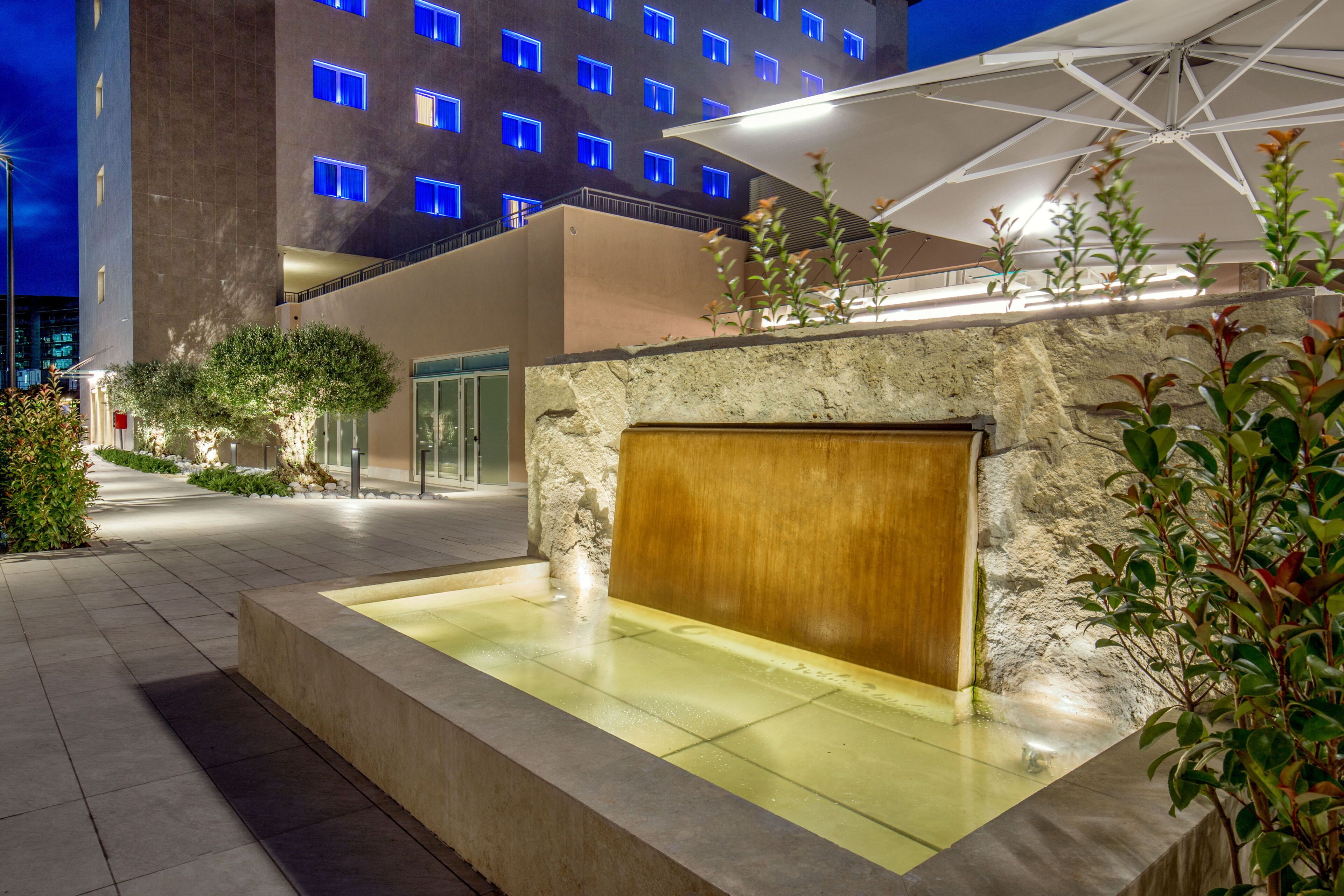 A modern hotel courtyard with a water feature, stone walls, and an umbrella.