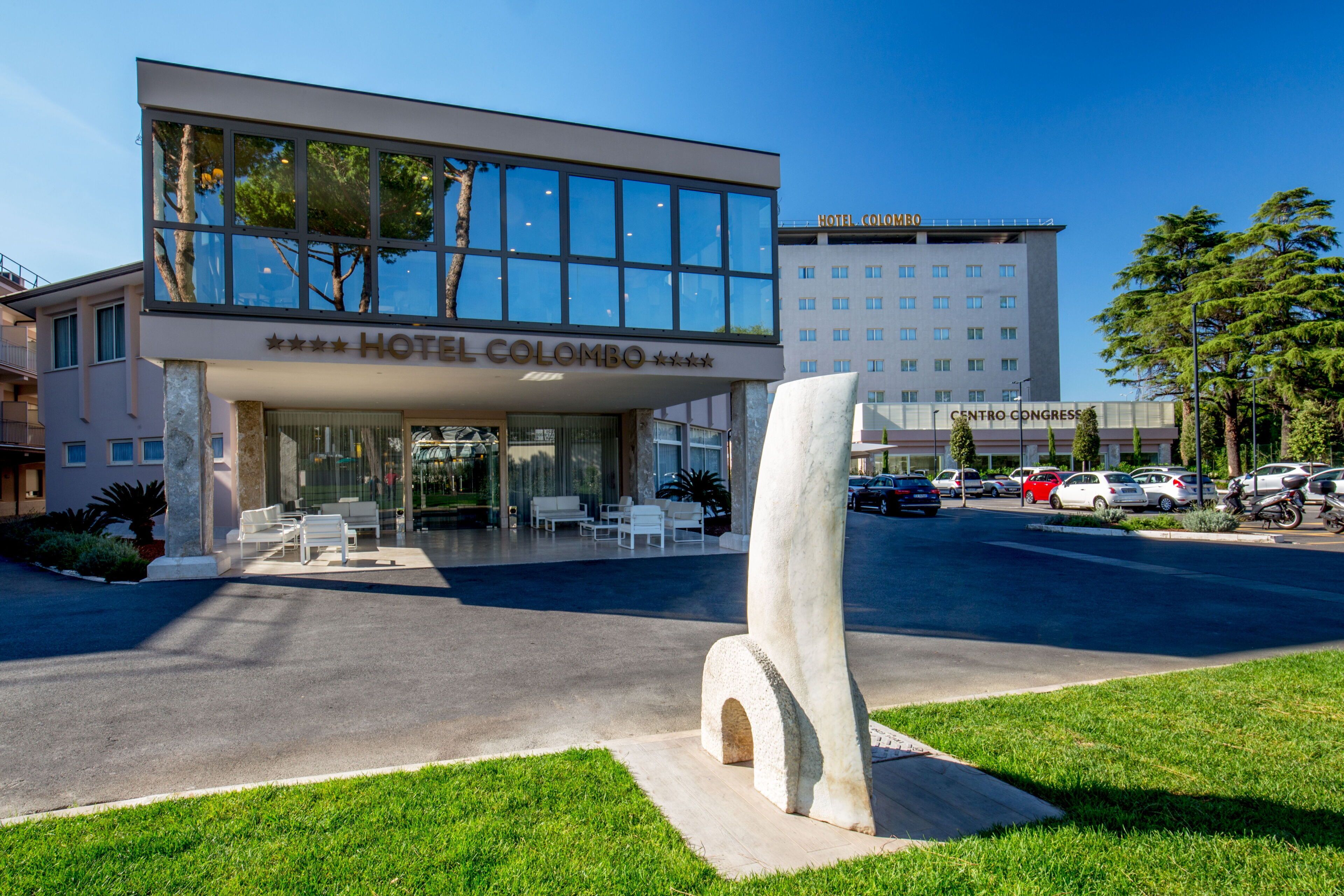 A modern hotel with a glass facade, a prominent entrance, and a parking area.