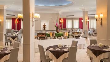 Comedor de hotel con mesas redondas, sillas y un bufé al fondo.