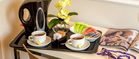 A tray with two cups of tea, a black kettle, a vase with yellow flowers, a bowl of snacks, and a magazine.