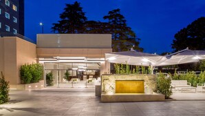 A modern hotel entrance with a glass facade, outdoor seating area, and a well-lit reception desk. - Hotel Cristoforo Colombo (Rome)