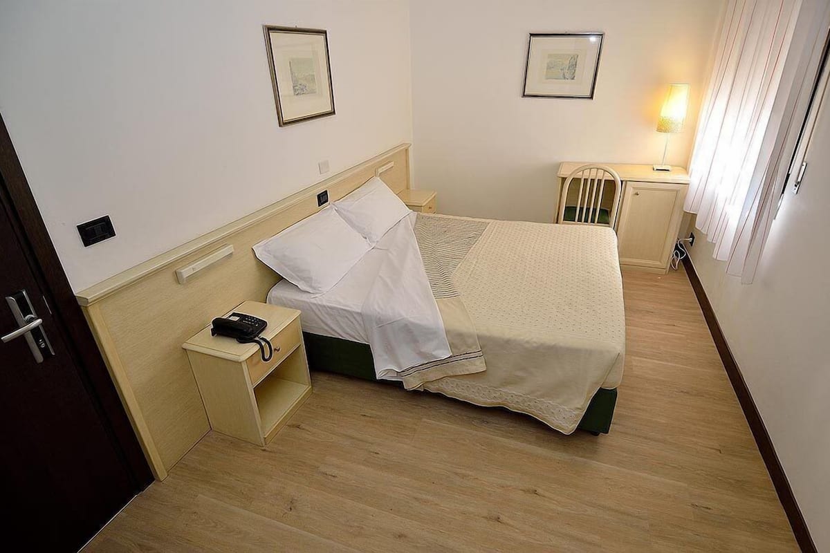 Una habitación de hotel con cama, mesita de noche, lámpara y cuadros en la pared.