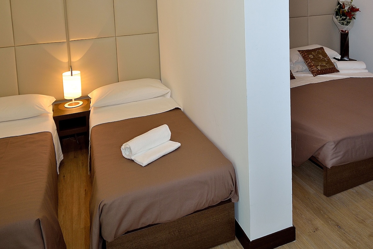 Habitación de hotel con dos camas, una mesita de noche con lámpara y un espejo grande.