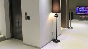 Un hall d’entrée moderne avec un lampadaire, un ascenseur et un écran de télévision diffusant une émission.